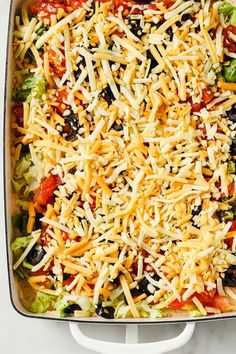 a casserole dish with cheese, olives, lettuce and tomatoes