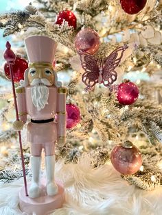 a pink nutcracker standing next to a christmas tree