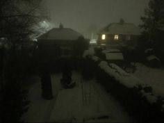 the snow covered yard is lit up by two lights in the distance, with houses and trees on either side