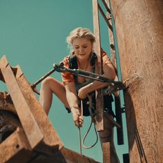 a woman climbing up the side of a wooden structure with an electric wire attached to it