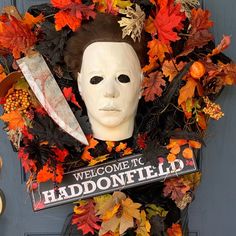 a halloween wreath with a mask, knife and sign on the front door that says welcome to haddonfield