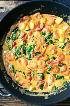 a skillet with shrimp, pineapples and spinach in it on a wooden table