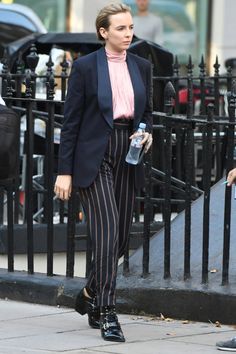 a woman walking down the street with a water bottle in her hand and wearing striped pants