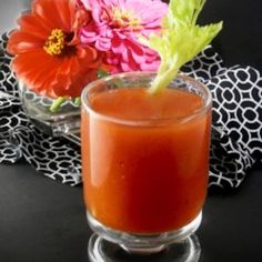 an orange drink sitting on top of a table next to a vase filled with flowers