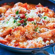 a close up of food in a bowl with shrimp and cheese on the top, garnished with basil