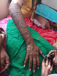 a woman getting henna done on her arm and hands with scissors in hand, while another woman is sitting down next to her