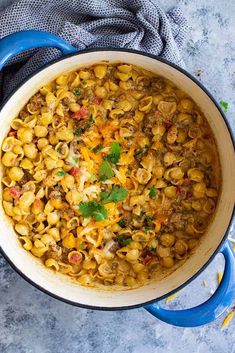 a pot filled with pasta and meat on top of a blue cloth next to a spoon