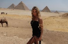 a woman standing in front of pyramids with a camel behind her on the desert