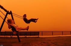 two children are playing on a swing set at the beach as the sun goes down