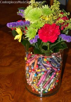 a vase filled with lots of colorful flowers and crayons on top of a wooden table