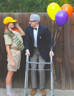 a man and woman dressed up in costumes standing next to a ladder with balloons on it