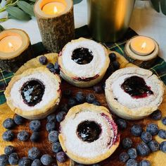 four blueberry pies on a table with candles