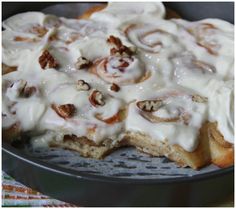 a pan filled with cinnamon rolls covered in icing and pecans on top of it