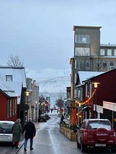 two people walking down the street in front of some buildings with christmas lights on them