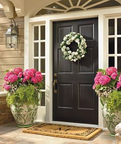 two flower pots with wreaths on the front door, and one is holding pink carnations