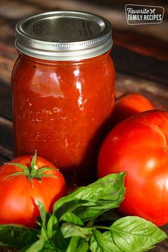 a jar filled with tomato sauce sitting on top of a table next to tomatoes and basil