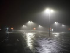 an empty parking lot at night with street lights shining on the foggy pavement and benches