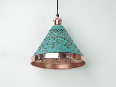 a copper and teal colored lamp hanging from a cord on a white wall background