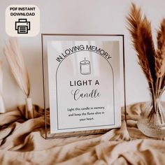 a glass vase with some brown feathers in it and a sign that says moving memory light a candle