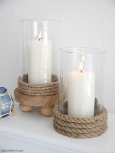 two white candles are sitting in glass vases on a shelf next to a rope wrapped candle holder