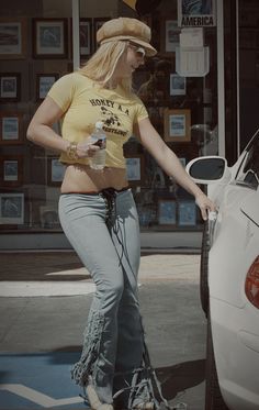 a woman is standing next to a car with her hand on the back door handle