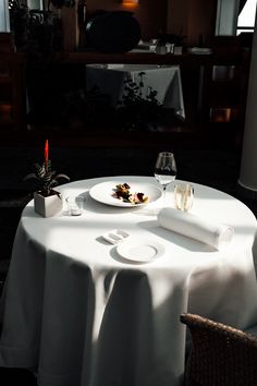 a white table topped with a plate of food next to a wine glass and candle