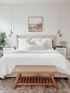 a bed with white linens and pillows in a large room next to a wooden coffee table