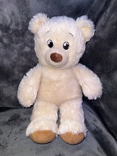 a white teddy bear with big eyes sitting on a gray background in front of a black backdrop