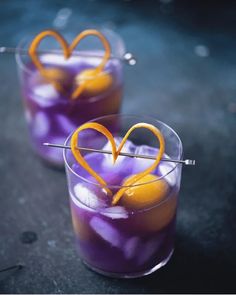 two glasses filled with purple liquid and orange garnish on top of each other