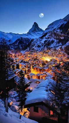 a snowy mountain town at night with the moon in the sky