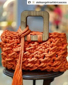 an orange crocheted bag with a wooden handle and tassell on top