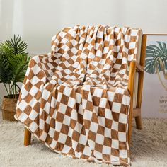 a brown and white checkered blanket sitting on top of a wooden chair next to a potted plant