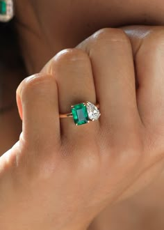 a woman's hand holding an emerald and diamond ring