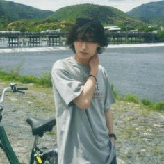 a young man standing next to his bike by the water with mountains in the background