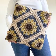 a woman is holding a crocheted pillow with flowers on the front and sides