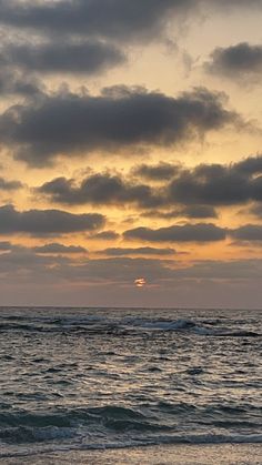 the sun is setting over the ocean with clouds in the sky and waves on the beach