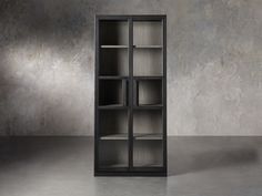 an empty black bookcase in front of a concrete wall with light coming through it