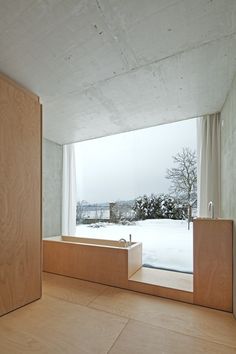 an empty room with a large window overlooking the snow covered yard and trees in the distance