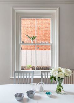 a white table with two vases and some flowers on it next to a window