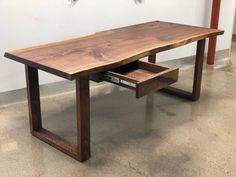 a wooden table with one drawer open on concrete flooring in front of a white wall