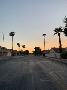 an empty street with palm trees on both sides and houses in the background at sunset