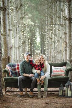 a man, woman and child sitting on a couch in the woods with christmas lights