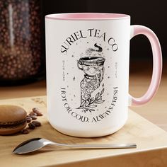 a pink and white coffee mug sitting on top of a wooden table next to a spoon