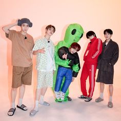 four young men standing next to each other in front of a pink wall wearing matching clothing