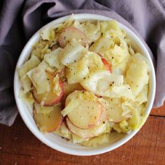 a white bowl filled with potato salad on top of a wooden table next to a gray napkin