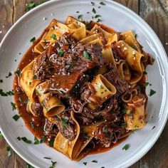 a white plate topped with pasta covered in meat and sauce on top of a wooden table