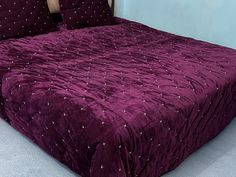 a purple bedspread with white stars on it in a room next to a blue wall