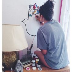 a person sitting on the floor with some paint and brushes in front of a lamp