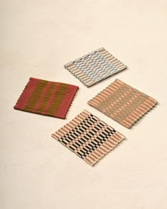 four pieces of woven material sitting on top of a white surface with pink and blue stripes