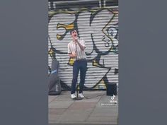 a man standing in front of a graffiti covered wall talking on a cell phone while holding his hand up to his mouth